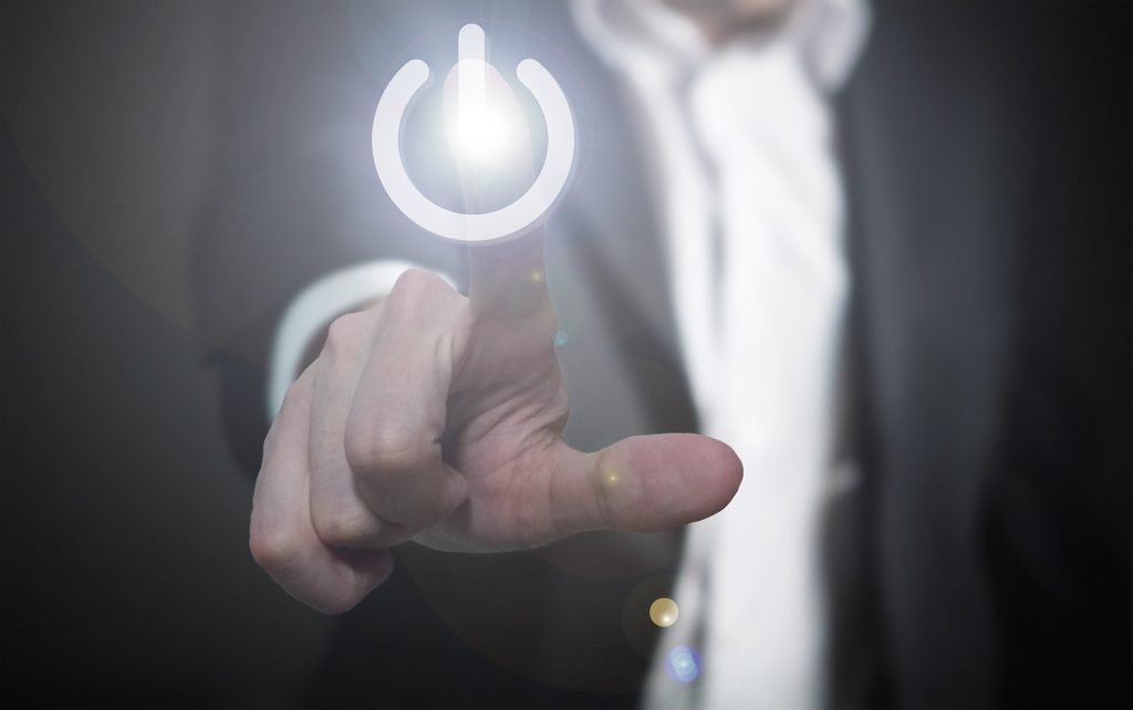 Photo of a person in professional clothing with their arm stretched out and their finger about to press a glowing power button icon to signify launching a new software product.